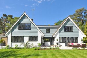 Modern family home exterior showcasing a large lawn and garden under a clear blue sky.