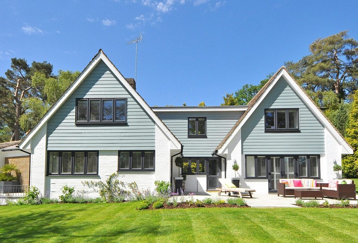 Modern family home exterior showcasing a large lawn and garden under a clear blue sky.