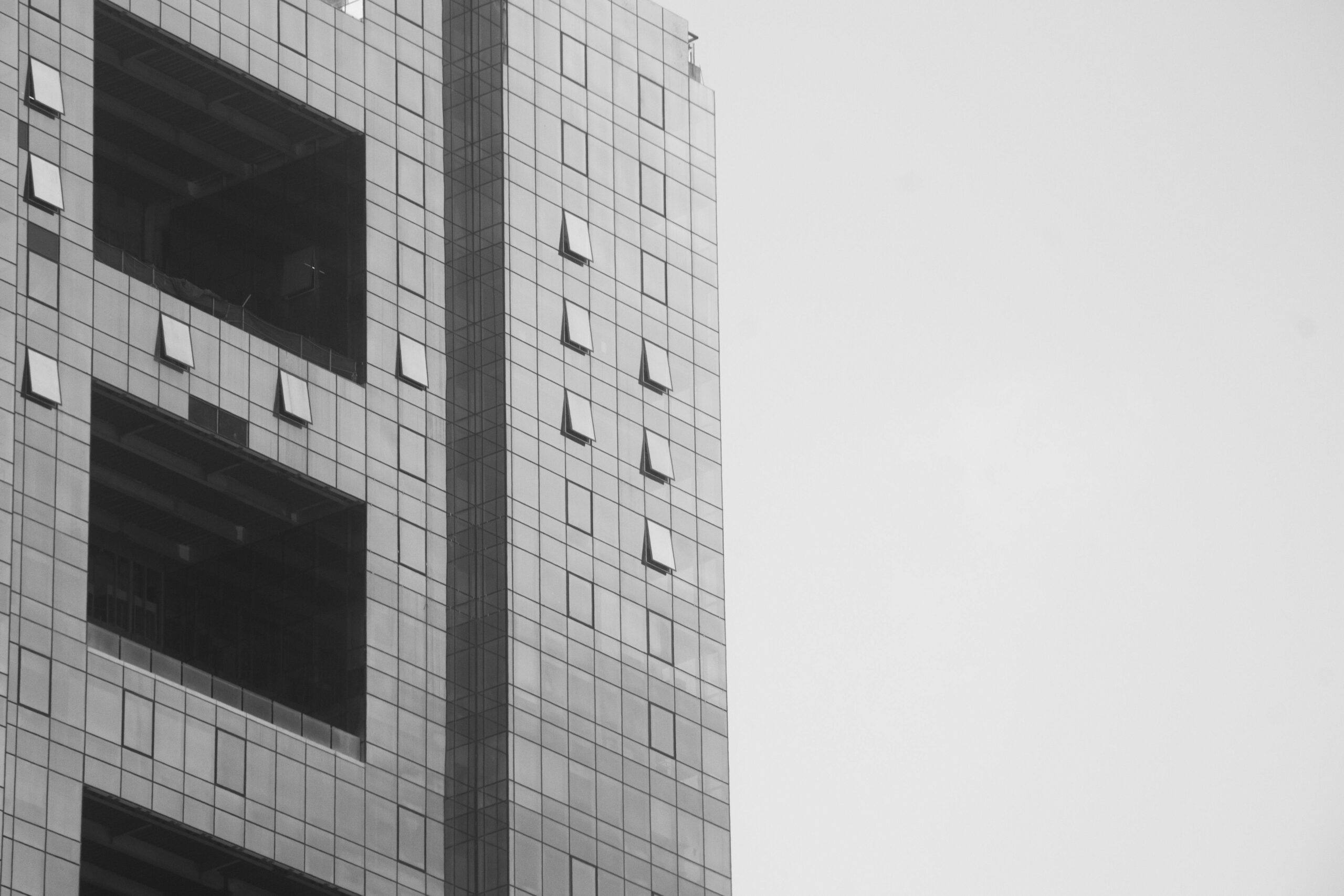 flat in mumbai Black and white image of a modern skyscraper facade in Mumbai, showcasing geometric design.