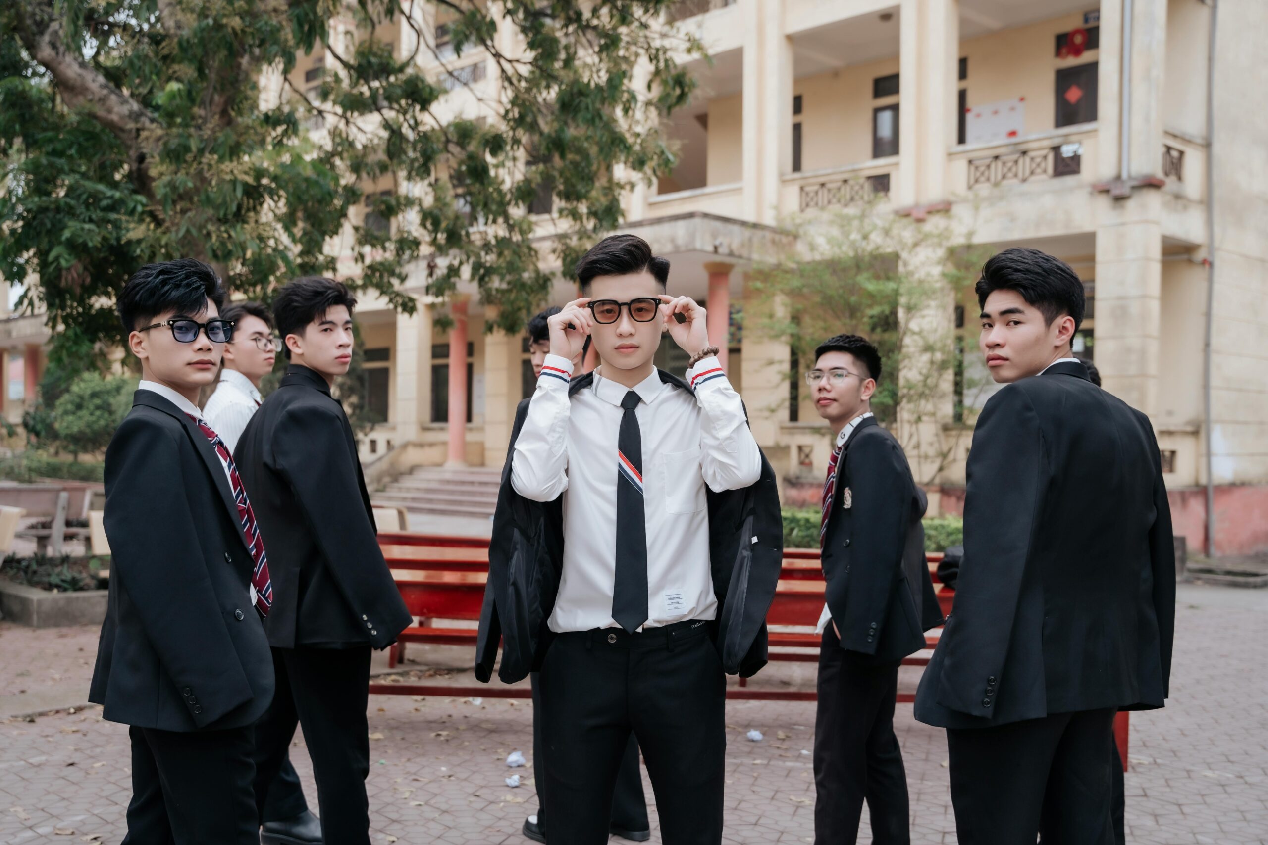 Six young men in formal suits and ties posing confidently outdoors.